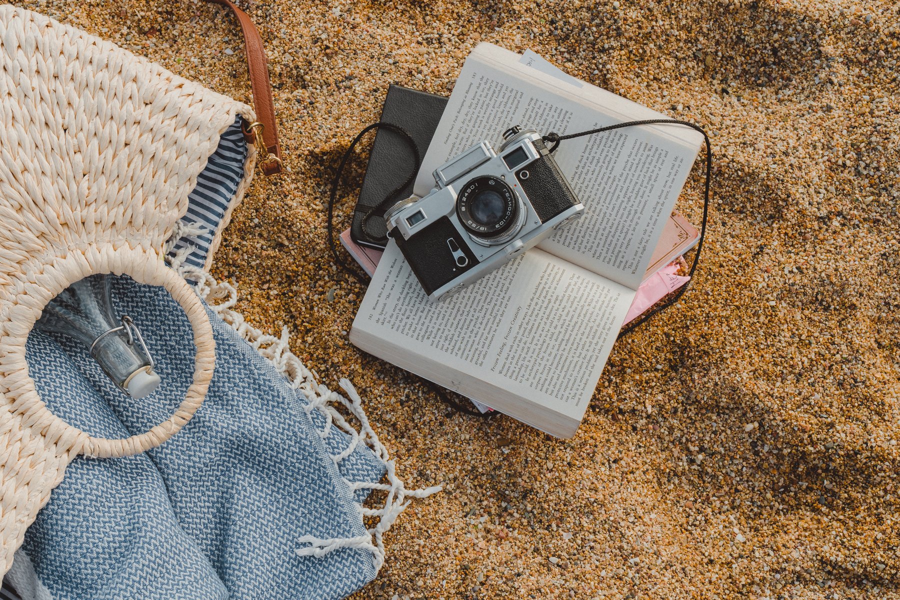 Composition of Beach Bag, Books, and Vintage Camera on Sand